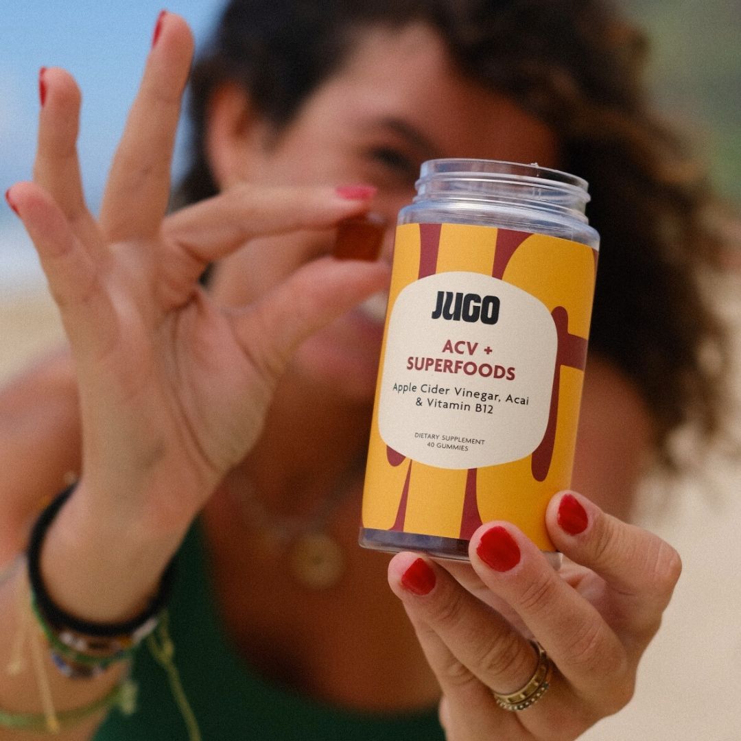 A person holds a Jugo ACV Superfoods gummy between their fingers, with the bottle visible in the background.