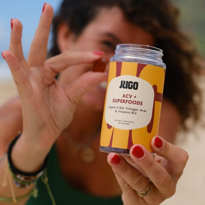 A person holds a Jugo ACV Superfoods gummy between their fingers, with the bottle visible in the background.