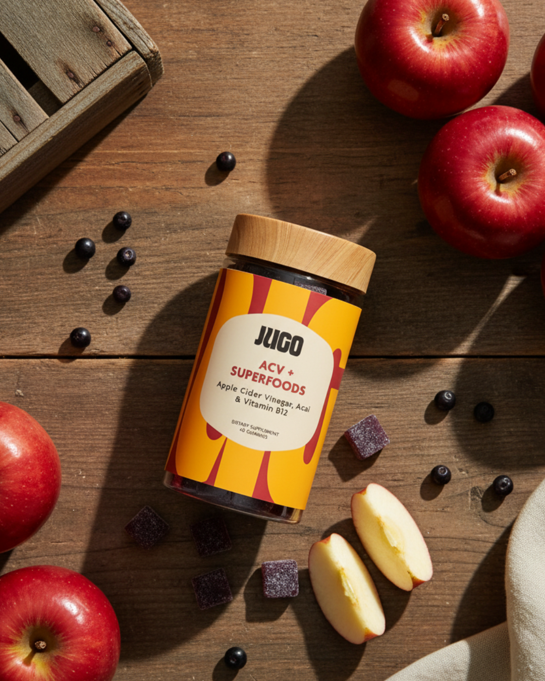 Top-down view of a Jugo ACV Superfoods bottle on a wooden surface with apples, apple slices, and scattered gummies.