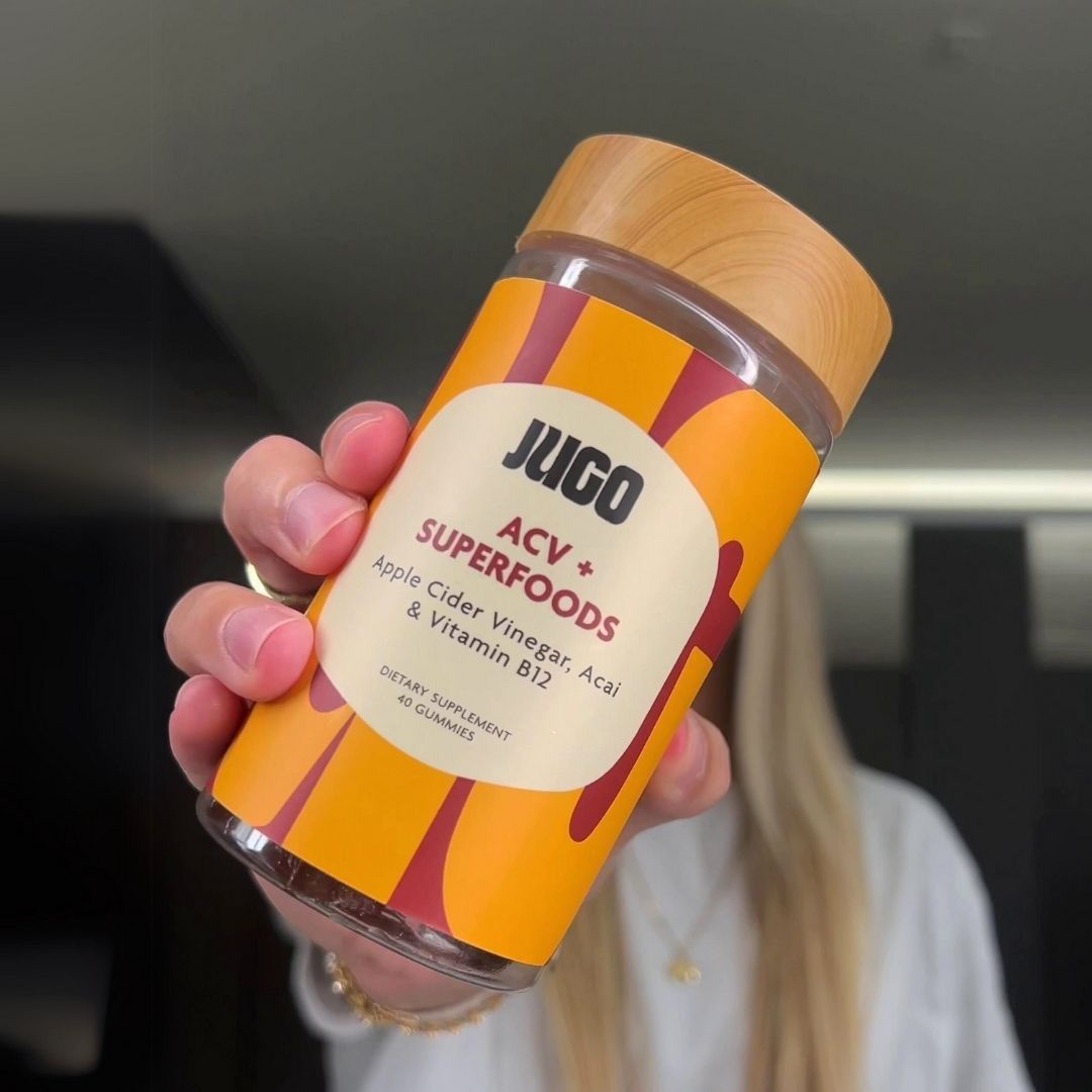 Close-up of a hand holding a bottle of Jugo ACV Superfoods gummies indoors, label facing the camera.